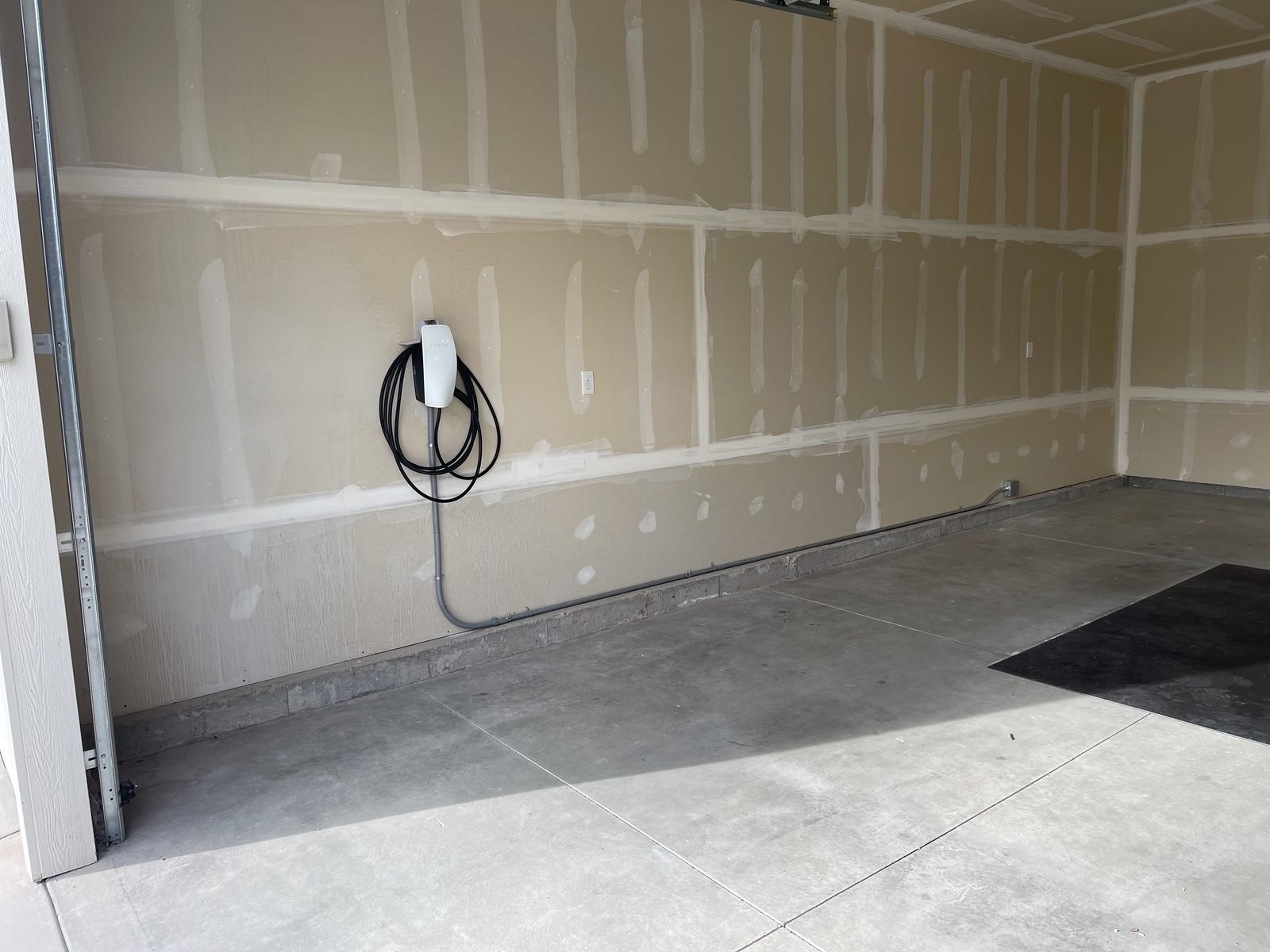 Tesla Wall Connector mounted on a garage wall with surface conduit run along the base